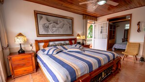 Un dormitorio con una cama grande, cabecera de madera, dos mesitas de noche con lámparas, un cuadro colgado en la pared y vistas a un balcón exterior.