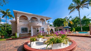 Una casa grande de dos pisos con un camino de entrada circular, una fuente y una zona de piscina.