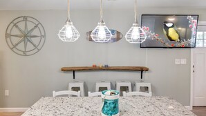 Een eetruimte met een houten balk boven een tafel, drie hanglampen, een wandgemonteerde televisie en een decoratief wandobject.