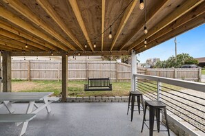 Une terrasse extérieure avec des poutres en bois, des guirlandes lumineuses, un banc et deux tabourets.