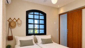 A bedroom with two beds, a ceiling fan, an air conditioning unit, a window with blinds, and a wooden door.