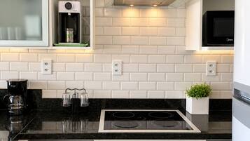 A kitchen with white cabinets, a black countertop, a built-in oven, a microwave, a blender, and a coffee maker.