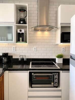 A kitchen with white cabinets, a black countertop, a built-in oven, a microwave, a blender, and a coffee maker.
