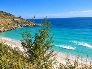 A coastal landscape with a clear view of the ocean, a sandy beach, and a rocky shoreline. - Charming apartment with AC and ocean view. (Arraial do Cabo)