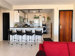 A modern kitchen with a central island, bar stools, and a red sofa in the foreground.