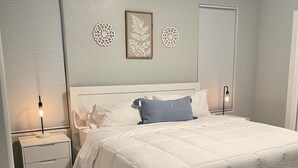 A bedroom with a large bed, white bedding, a nightstand with a lamp, and decorative wall art. - NEW! Heart of Downtown: The Hill Oasis (Grand Junction)