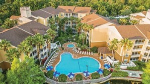 Ein Resort mit einem zentral gelegenen Swimmingpool, umgeben von Palmen und Liegestühlen.