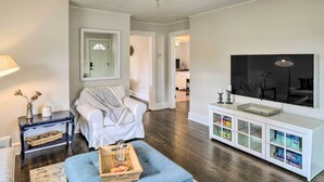 Ein Wohnzimmer mit weißem Sofa, blauem Hocker, dunklem Couchtisch, weißen Sideboard mit Glastüren und Deckenventilator.