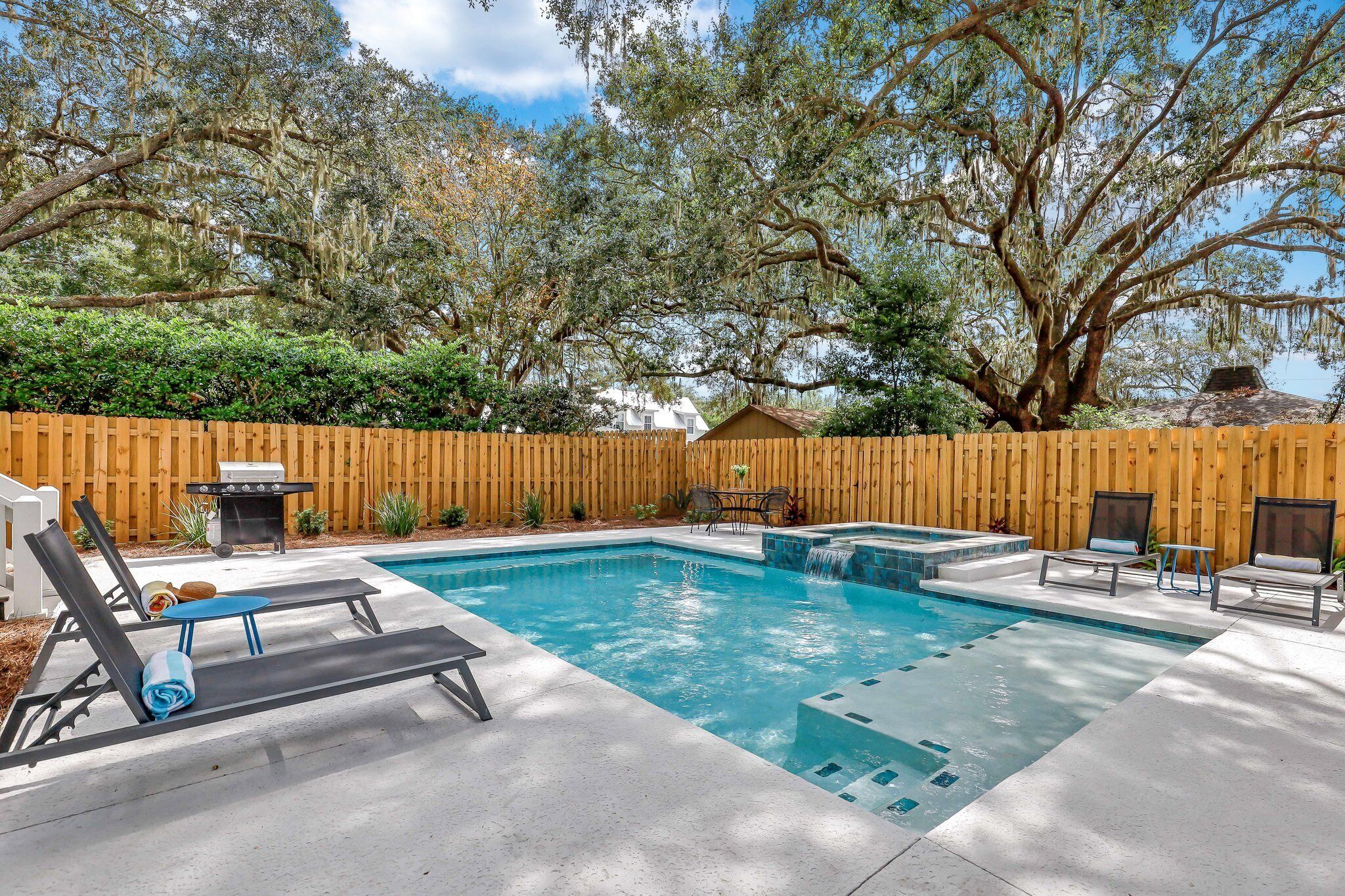 Un jardin avec une piscine, des chaises longues, un barbecue et une clôture en bois.