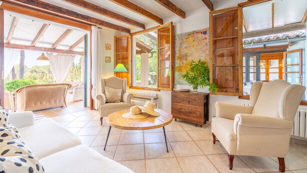 A spacious living area with a sofa, armchairs, a coffee table, and a dining table. There is a large window with curtains, a plant, and a lamp. - Ca na Tinta - with private swimming pool (Algaida)