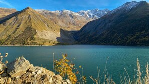 Un paysage montagneux avec un lac aux eaux limpides, un premier plan rocheux et des sommets enneigés en arrière-plan.