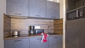 Una cucina compatta con mobili scuri, un forno a microonde, un tostapane e una macchina da caffè.