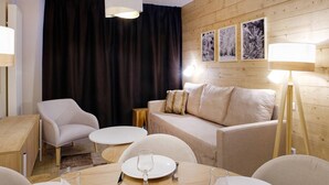 Una habitación de hotel moderna con detalles de madera, un sofá, dos sillones, una mesa de comedor con un vaso y una lámpara.