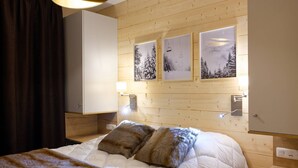 A bedroom with a bed, two pillows, a blanket, wooden walls, and three framed pictures on the wall.
