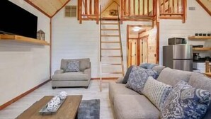 Ein gemütliches Wohnzimmer mit einer Couch, einem Couchtisch und einem Fernseher. Eine Treppe führt zu einer Schlafkoje.