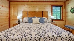 Ein Schlafzimmer mit Holzwandverkleidung, einem großen Bett, zwei Nachttischen und einem Fenster mit Jalousien.