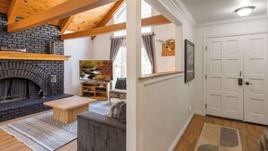 Une pièce avec une cheminée, des poutres en bois, un canapé, une table basse, un tableau et une porte.