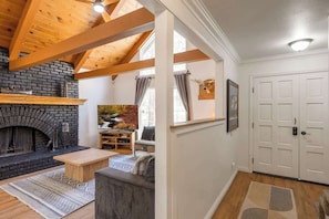 A room with a fireplace, wooden beams, a sofa, a coffee table, a painting, and a door.