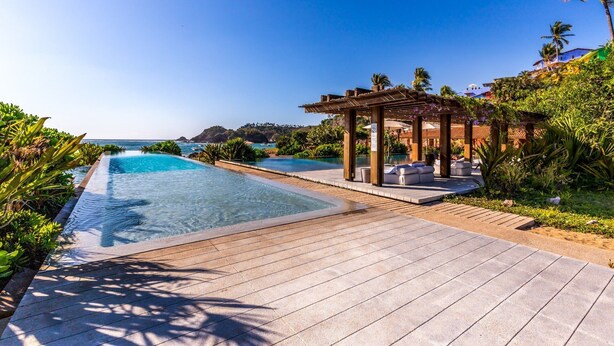 Ein Poolbereich eines Resorts mit zwei separaten Pools, einer Holzterrasse und einem überdachten Sitzbereich.