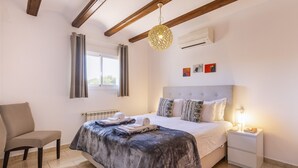 Een slaapkamer met een bed, een stoel, een nachtkastje en een hanglamp.