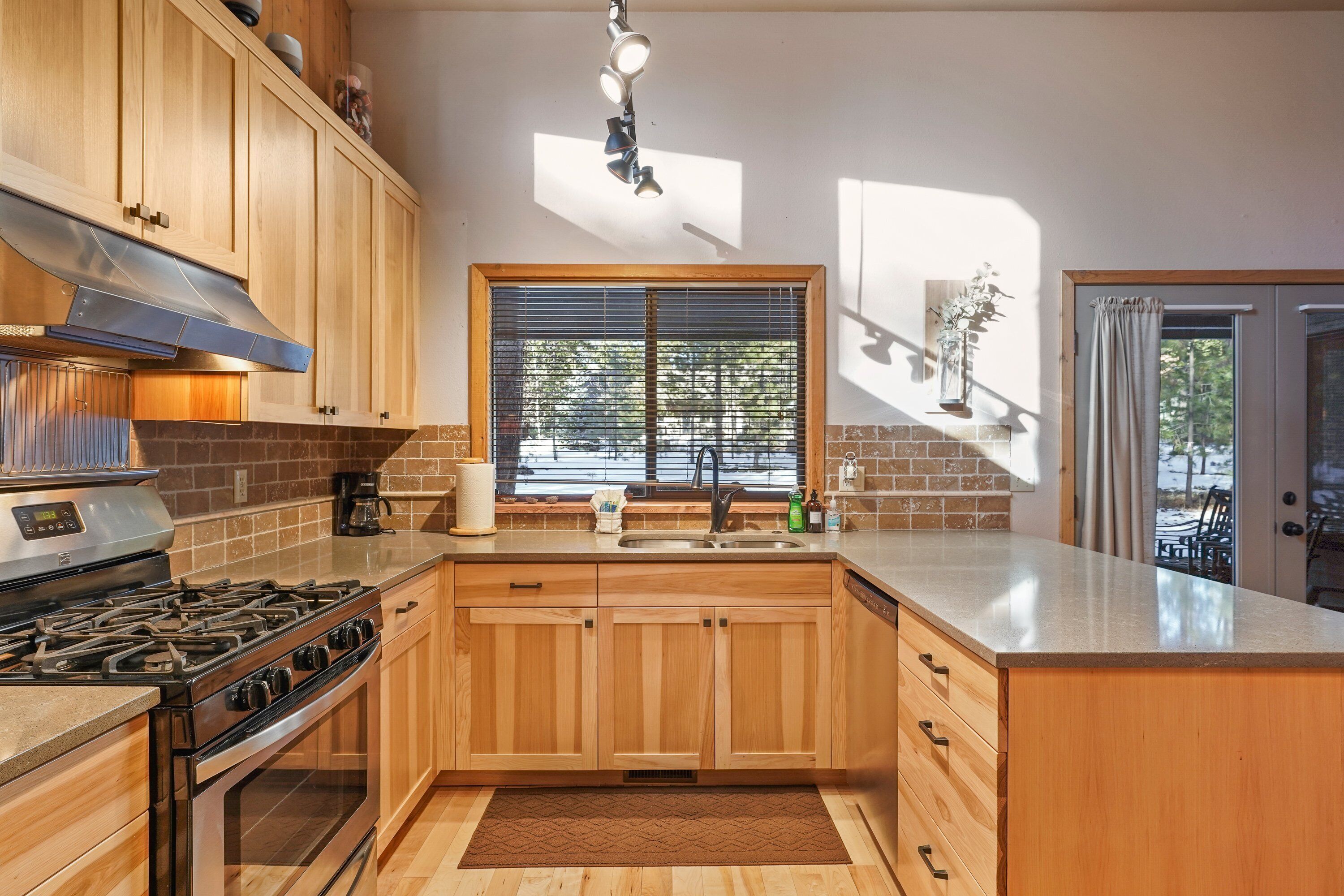 A kitchen with wooden cabinets, a gas stove, a sink, and a window with blinds.