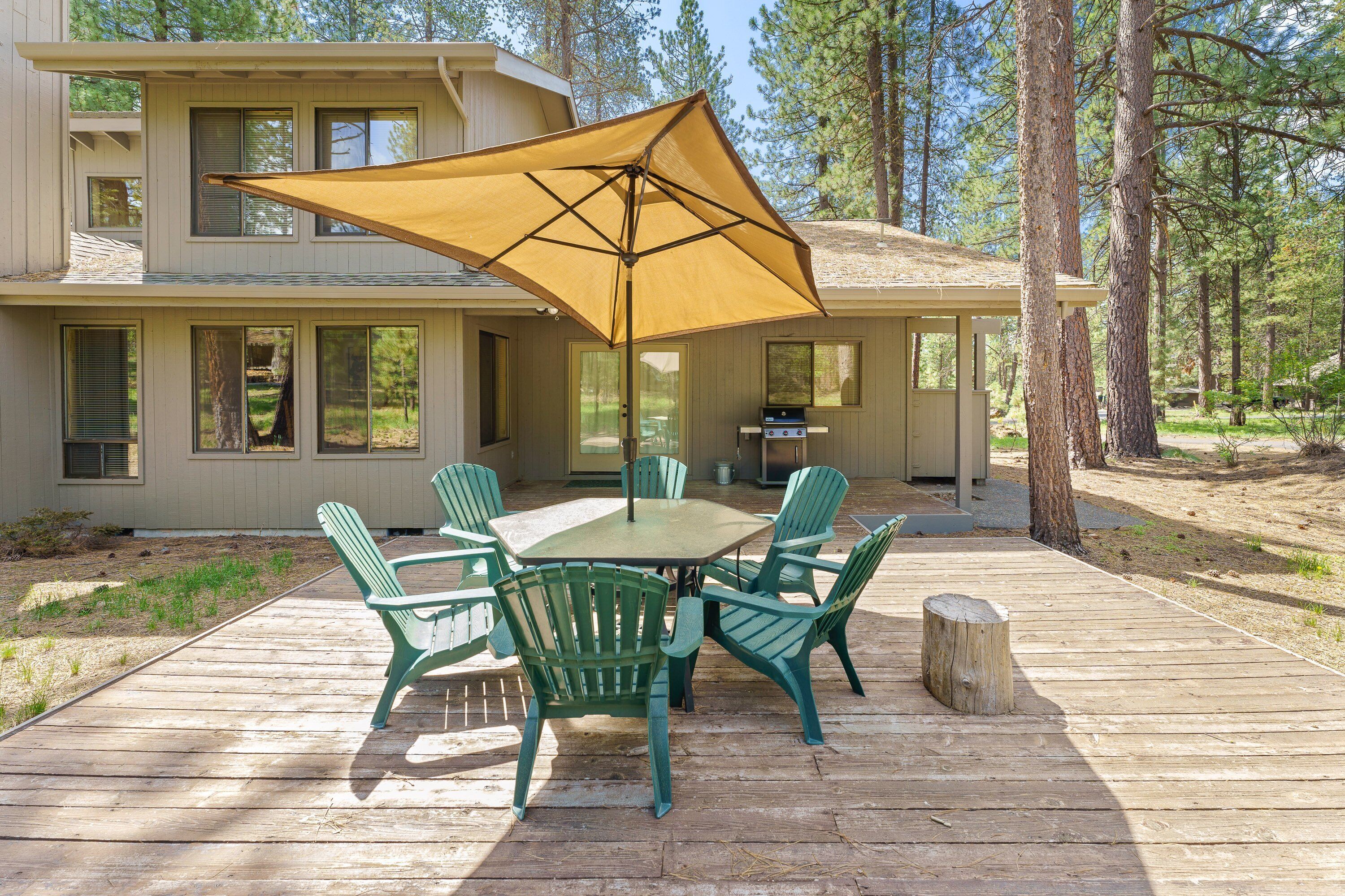 A deck with a table and chairs, a large umbrella, and a building with multiple windows in the background.