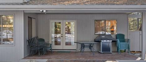 A covered patio with outdoor furniture, a grill, and a door leading to the house.