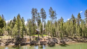 A lakeside lodge with a wooden deck and a clear view of the surrounding forest. - 110 Crane - Spectacular River Front + Access, Hot Tub, Ping Pong, South of Sunriver Resort (Sunriver)