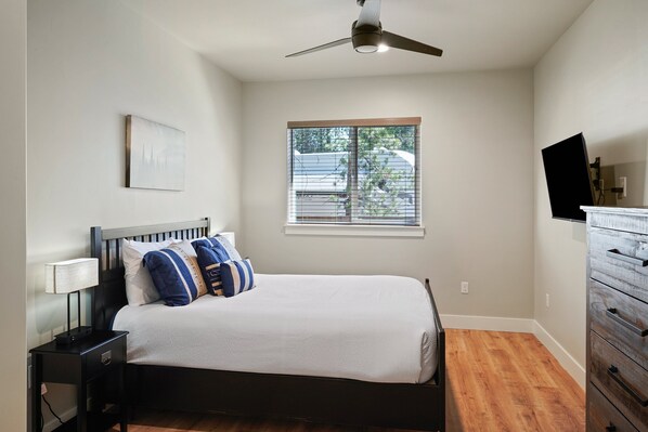 A bedroom with a bed, a nightstand, a dresser, a ceiling fan, a window, and a television. - 110 Crane - Spectacular River Front + Access, Hot Tub, Ping Pong, South of Sunriver Resort (Sunriver)