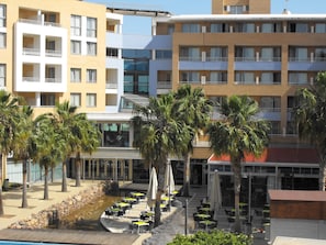 Ein Hotel mit mehreren Etagen, einer Sitzterrasse mit Sonnenschirmen und Palmen.