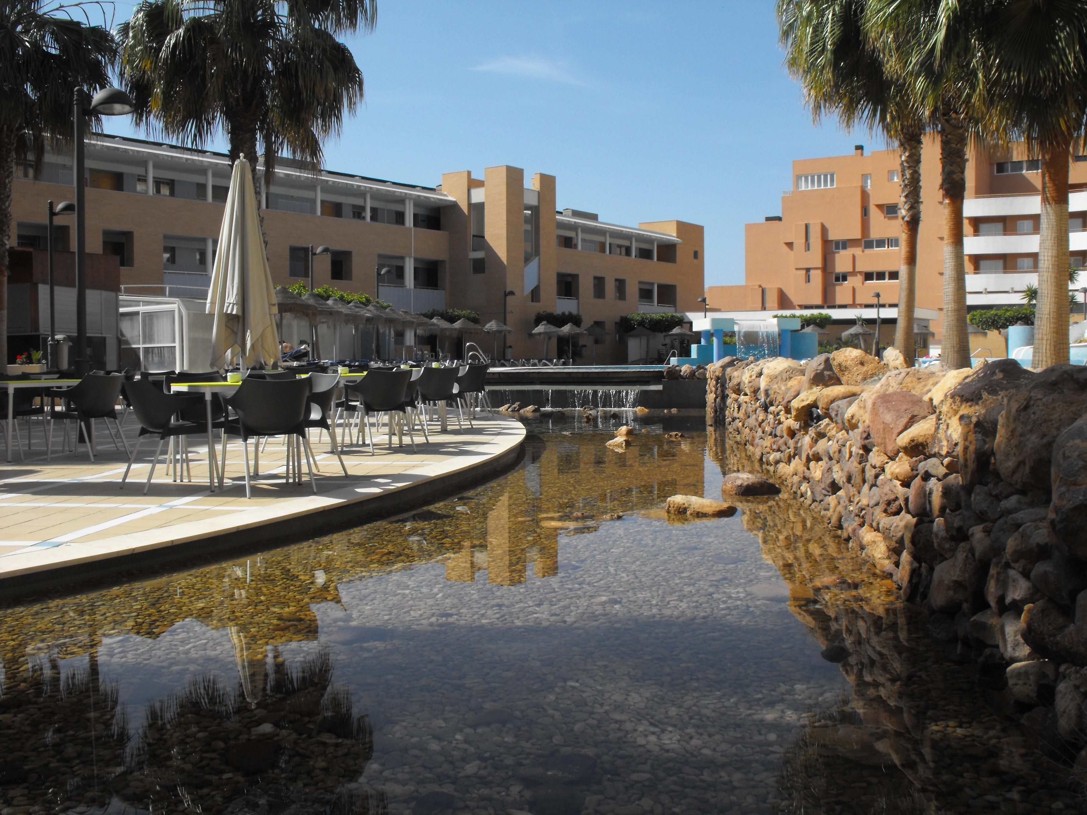 Zona de piscina amb mur de pedra, mobiliari exterior i un edifici al fons.