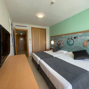 Habitación de hotel con dos camas, televisión, una mesa de madera y un mural en la pared.