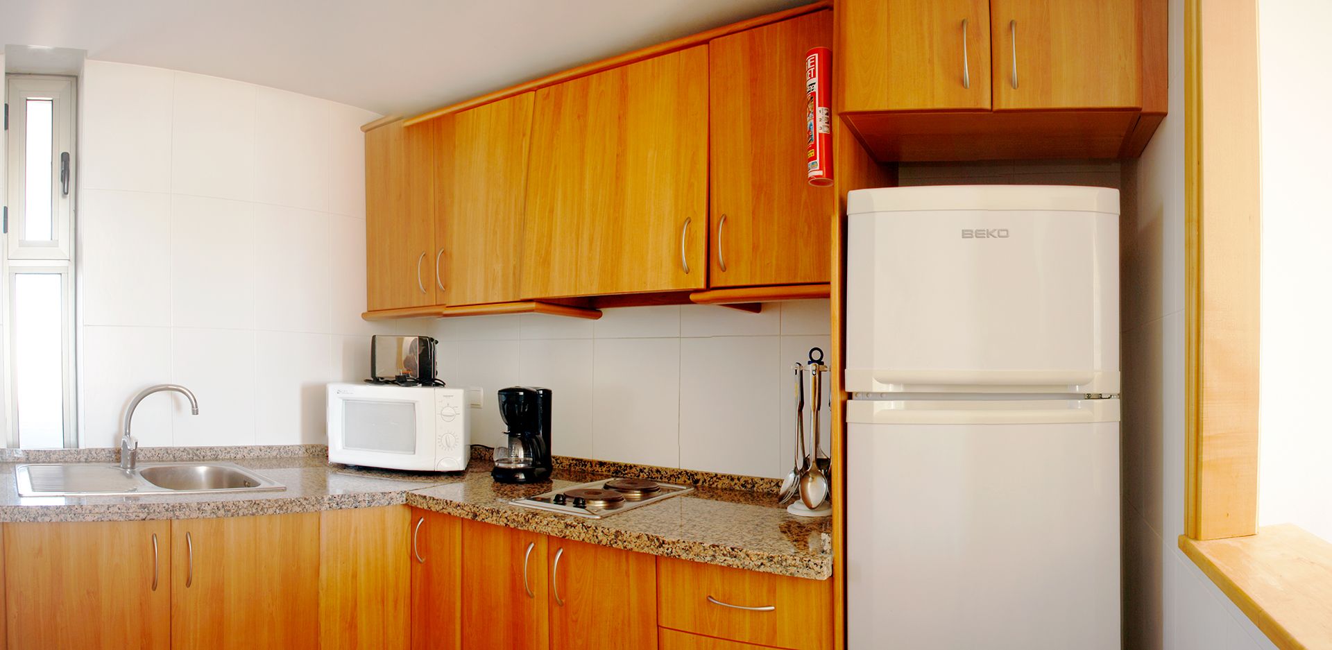 Une cuisine avec des meubles de rangement en bois, un réfrigérateur blanc, un four à micro-ondes, un grille-pain et une machine à café.