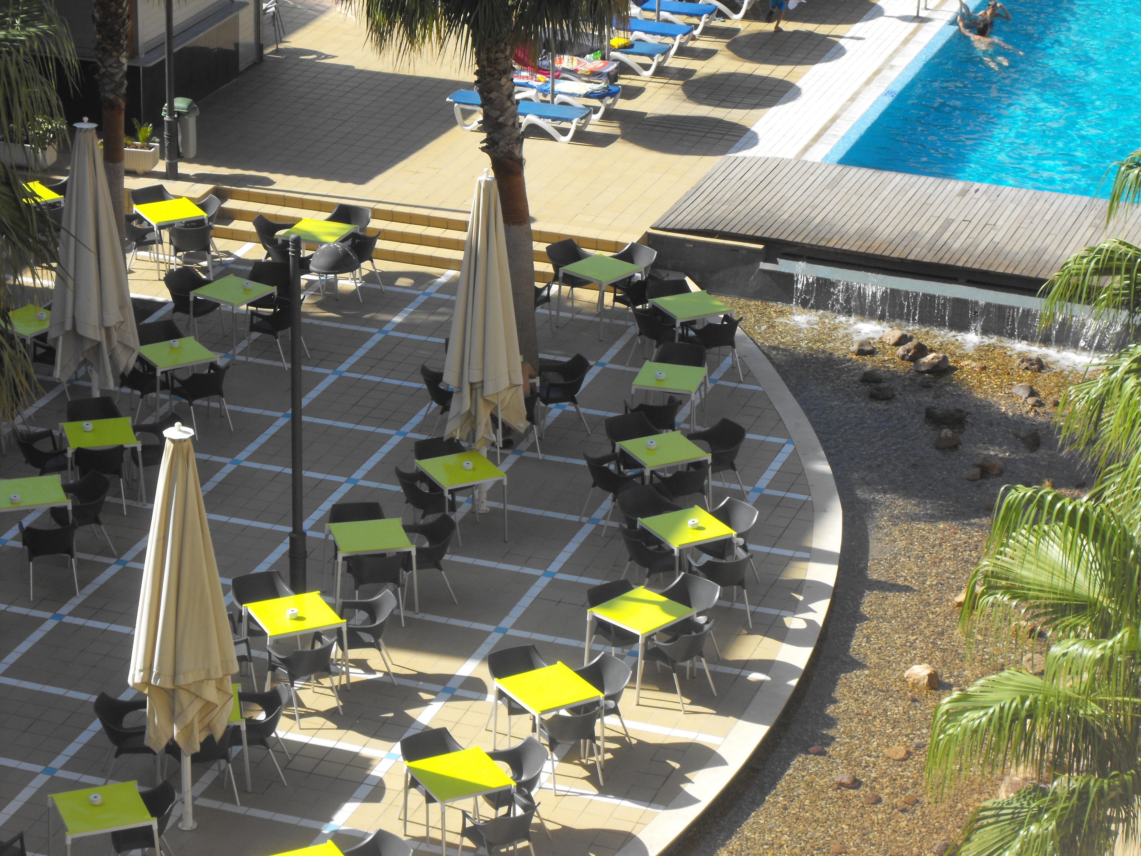 A poolside area with multiple tables and chairs, a pool, and a waterfall feature.