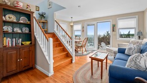 Un salón amplio con una escalera de madera, un sofá azul y un comedor con vistas al océano.