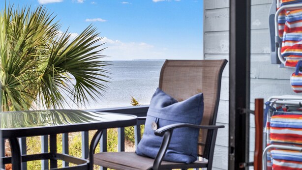 A balcony with a view of the ocean, a chair, a palm plant, and beach towels hanging on the wall. - Beautiful Water Views, Steps to Beach (Tybee Island)