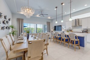 Una cocina moderna con armarios blancos, una isla azul y un comedor con mesa y sillas de madera.
