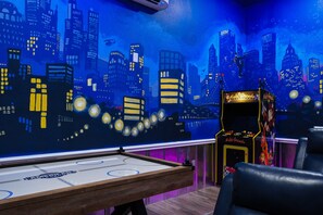 Una habitación con mesa de juego de discos, jukebox y un mural de un horizonte urbano.