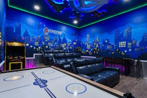 Una habitación con mesa de billar, asientos de cuero y un mural que representa un paisaje urbano con la marca 'Avengers'.