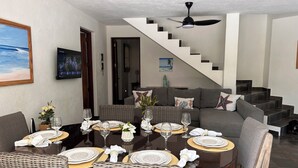A dining area with a round table set for six, surrounded by wicker chairs. There is a staircase leading to an upper level. - Quaint Villa with Beautiful gardens (Playa Encuentro)