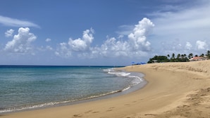 A sandy beach with clear blue water, a few umbrellas, and a structure with a red roof in the background. - Quaint Villa with Beautiful gardens (Playa Encuentro)