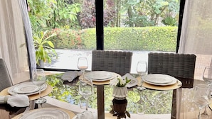 A dining area with a table set for four, featuring wicker chairs, white plates, and clear glassware. - Quaint Villa with Beautiful gardens (Playa Encuentro)