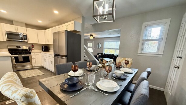 A modern kitchen with white cabinets, stainless steel appliances, and a dining area set for six with a long table. - Incredible 5 bed 2 bath w/ HOT TUB close to Pitt (Bethel Park)