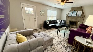 A living room with a grey sofa, a purple armchair, a glass coffee table, and a fireplace. - Incredible 5 bed 2 bath w/ HOT TUB close to Pitt (Bethel Park)