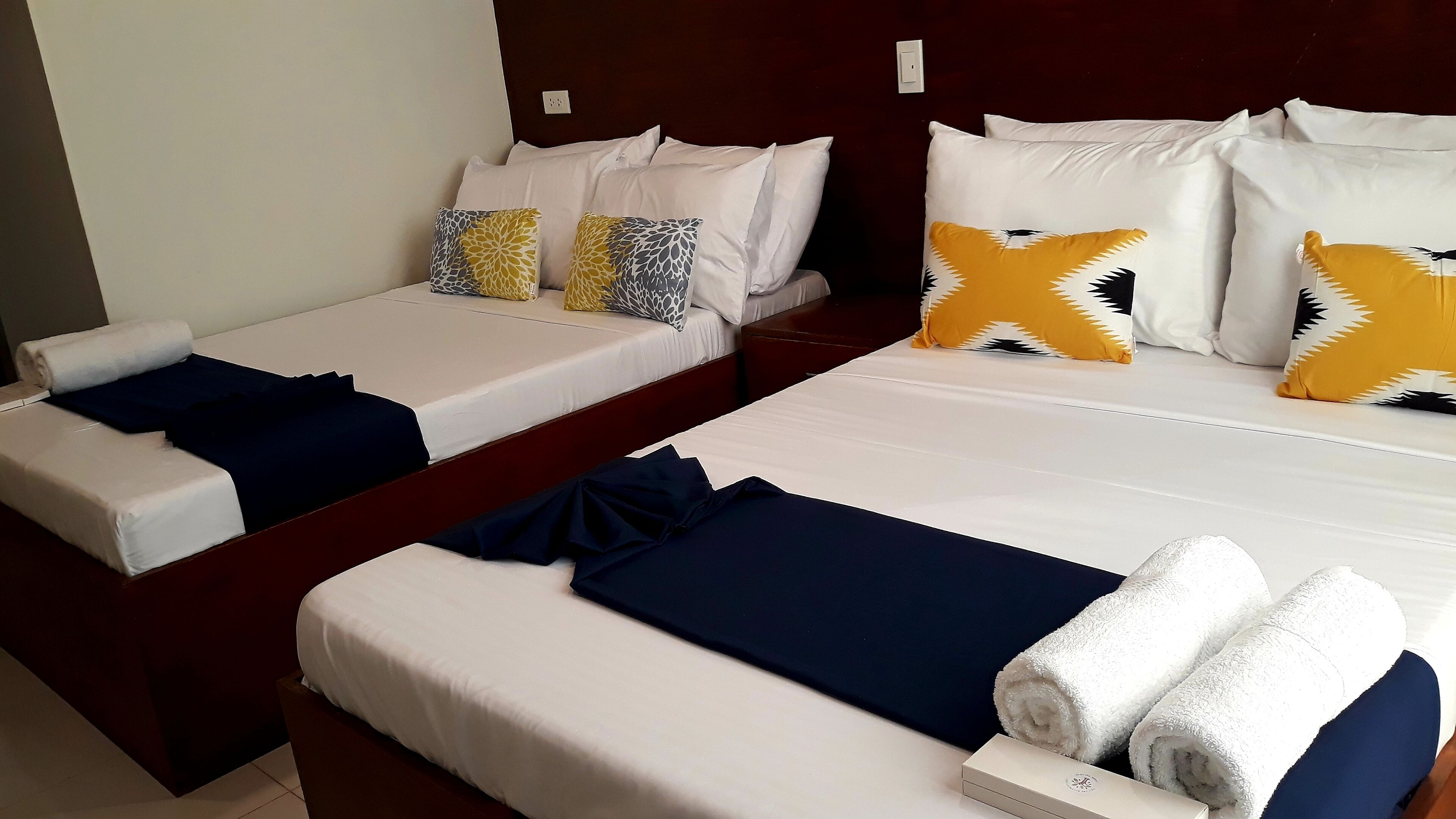 Two single beds with white linens, navy blue blankets, and decorative pillows in a hotel room.