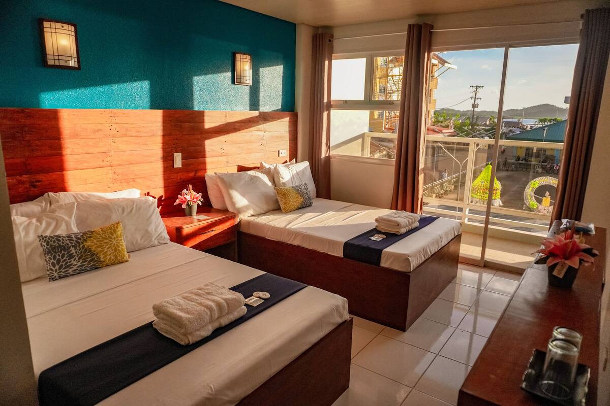 A hotel room with two beds, a wooden headboard, a large window with a view, and a small table with a vase.