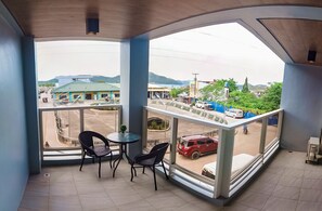 A balcony with a view of a street, a red car, and a building with a green roof. - A&A ABE BAYFRONT INN (Coron)