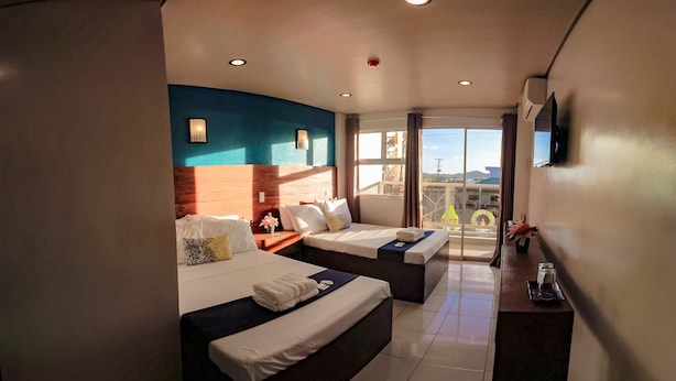 Habitación de hotel con dos camas, televisión, balcón con vistas y ventana con cortinas.