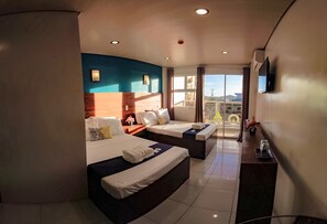 Ein Hotelzimmer mit zwei Betten, einem Fernseher, einem Balkon mit Blick und einem fenster mit Vorhängen.