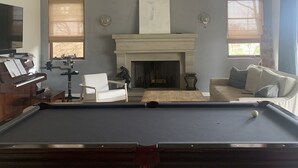 A spacious living room with a pool table, a fireplace, a piano, and a television.